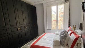 A bedroom with a large bed, dark wardrobe, and a window with a view of buildings. - Villa Zecca, Taormina (Taormina)