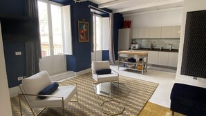 A modern living room with a sofa, a glass coffee table, and a patterned rug. There is a kitchen area with cabinets and a countertop visible in the background. - Villa Zecca, Taormina (Taormina)