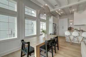 Une cuisine moderne dotée de grandes fenêtres, un coin repas avec une table et des chaises en bois, et un luminaire suspendu.