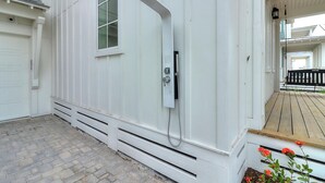 A white building with a covered porch, a window, and a showerhead.