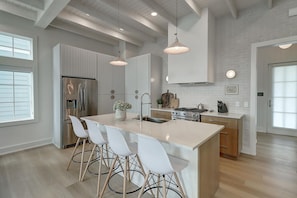 Une cuisine moderne dotée d’un îlot central, de meubles blancs, d’appareils électroménagers en acier inoxydable et de luminaires suspendus.