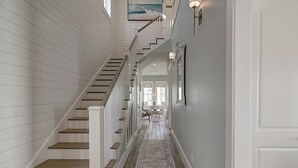 A hallway with a wooden staircase, white walls, and a patterned rug. - Surf & Sand 235 LAK (Port Aransas)