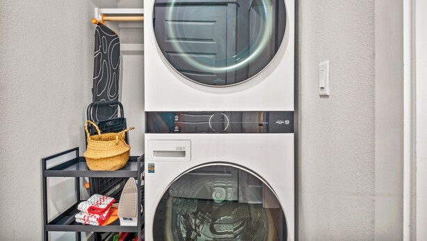 A laundry room with two stacked washing machines and a shelf with a basket and folded clothes. - Five O'clock Somewhere 205 Fiv-e (Port Aransas)