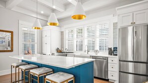 A modern kitchen with a large island, white cabinetry, stainless steel appliances, and pendant lighting. - Five O'clock Somewhere 205 Fiv-e (Port Aransas)