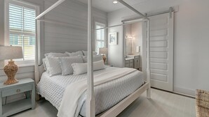 A bedroom with a four-poster bed, a nightstand with a lamp, a dresser, and a mirror. - Grand Central 226 GR (Port Aransas)