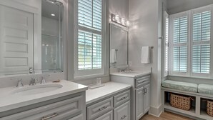 A modern bathroom with two sinks, a large mirror, and a bench with baskets. - Grand Central 226 GR (Port Aransas)
