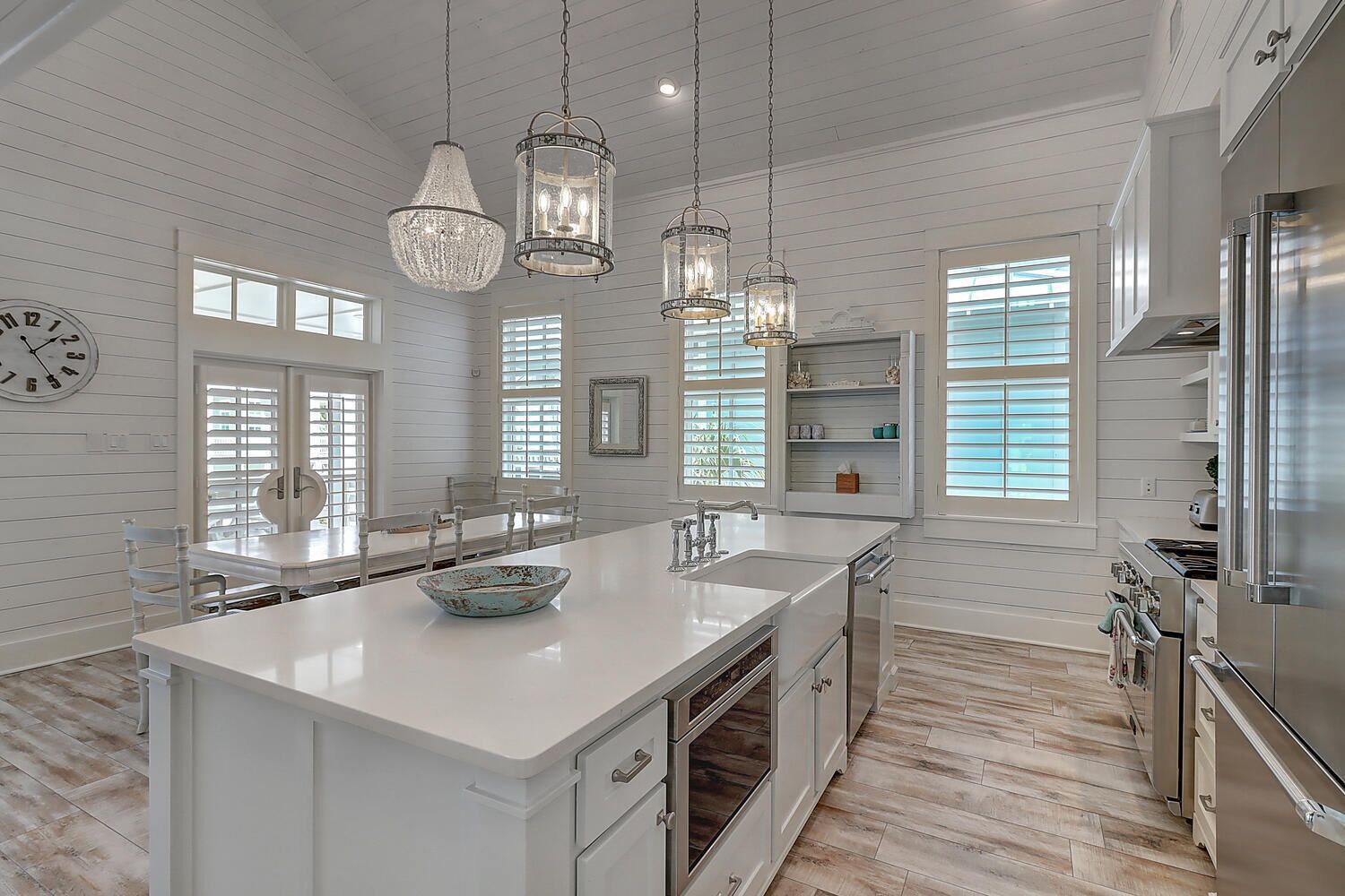 A spacious kitchen with white cabinetry, a large island, pendant lights, and a view of the outdoors through large windows.
