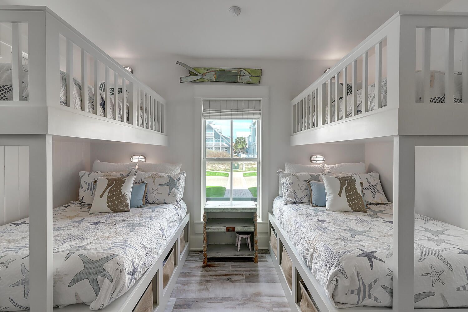Habitación con dos literas, cada una con ropa de cama temática de estrellas de mar, una mesita pequeña y una ventana con persianas.