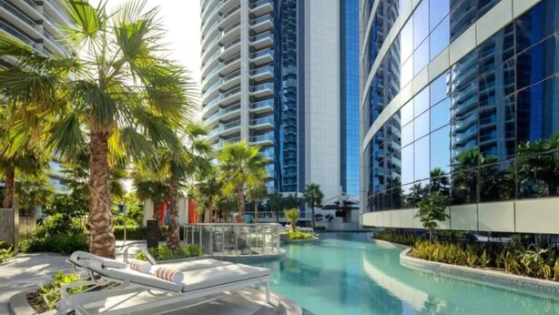 A modern hotel with a pool area, palm trees, and high-rise buildings in the background. - Paramount Towers 2BR Luxurious Apartment - 360 vacation (Dubai)