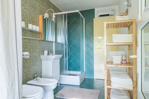 Un baño con ducha, inodoro, lavamanos y repisas con toallas.
