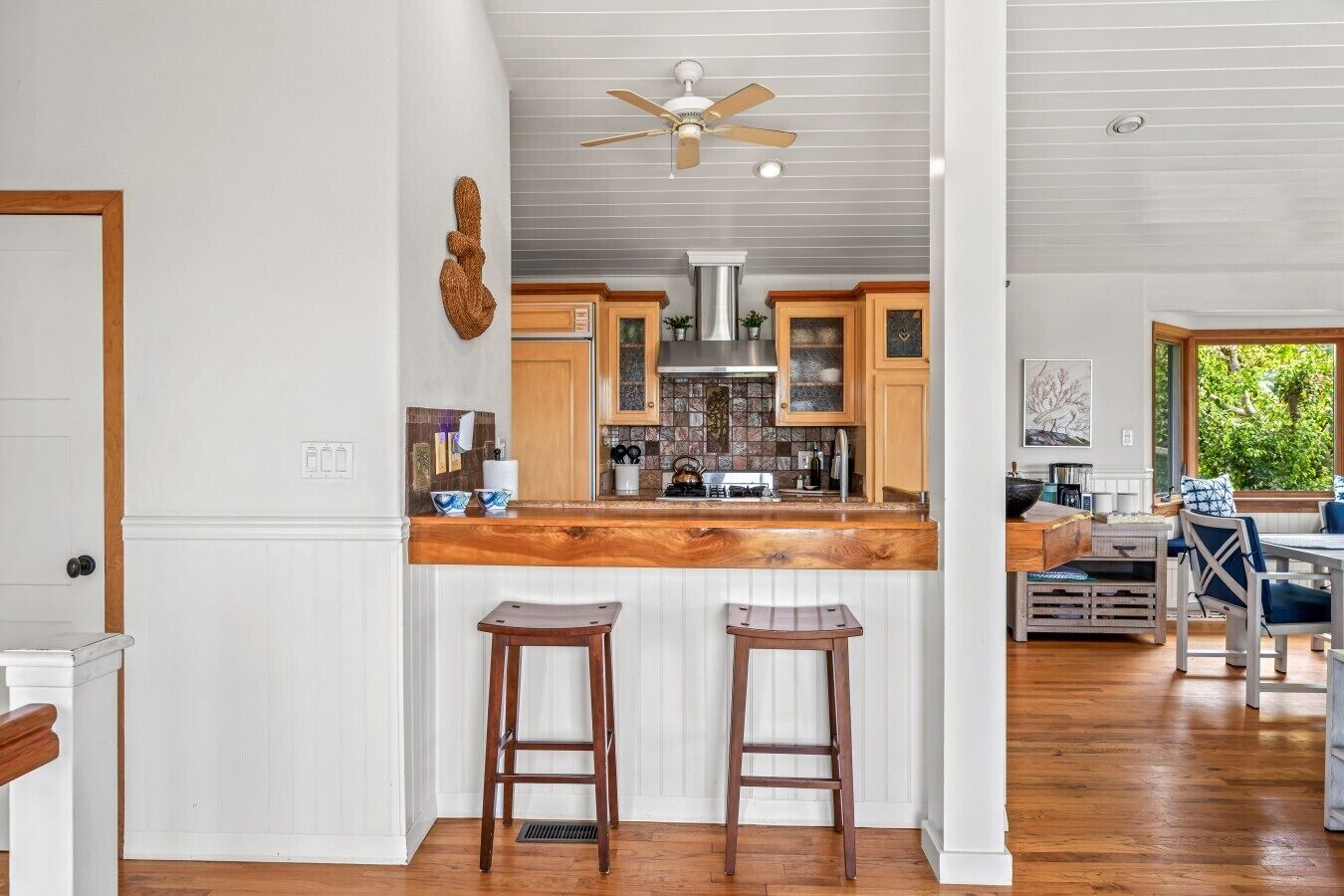 A kitchen with a wooden countertop, two stools, a ceiling fan, and a view of the outdoors through a window.