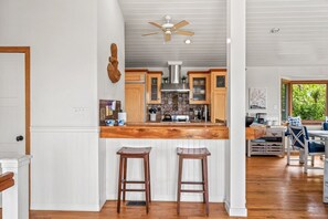Una cocina con encimera de madera, dos taburetes, un ventilador de techo y vistas al exterior a través de una ventana.