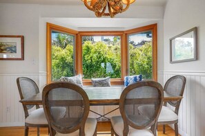 A dining area with a bay window, wicker chairs, and a wooden table.