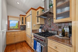 A kitchen with wooden cabinets, a gas stove, a refrigerator, and a window with a view.