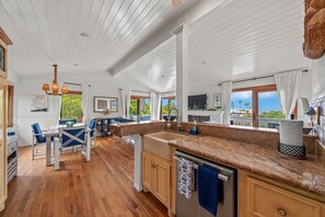 A spacious kitchen with a wooden floor, a large island with a sink, and a view of the outdoors. - Darling Beach Cottage, Ocean Views, central (Del Mar)