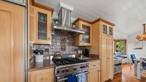 A kitchen with wooden cabinets, a stainless steel stove, and a tiled backsplash. - Darling Beach Cottage, Ocean Views, central (Del Mar)