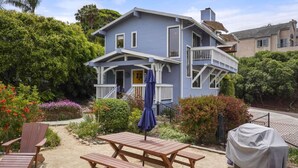 A two-story house with a porch, a covered patio, and a sandy garden area. - Darling Beach Cottage, Ocean Views, central (Del Mar)