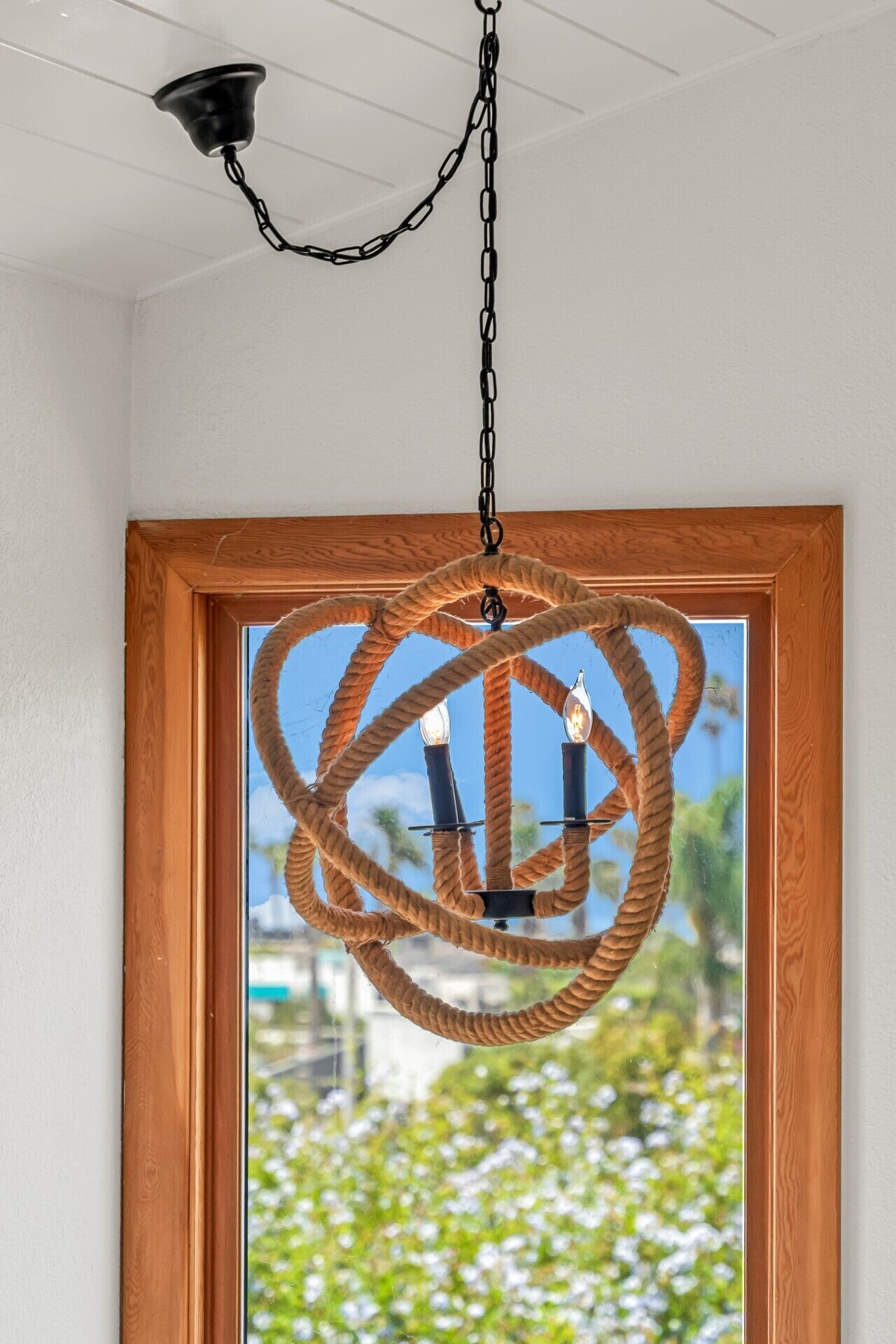 Un luminaire suspendu au plafond, muni d’une chaîne et doté d’un cadre de porte en bois avec une fenêtre.