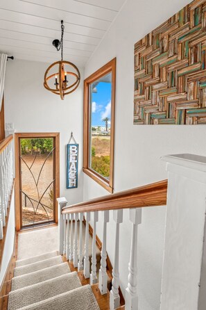 Una escalera con balaustres blancos y barandillas de madera que lleva a una puerta con vista a la playa.
