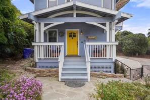 A two-story house with a bright yellow front door, a porch with white railings, and a stone pathway leading to the entrance.