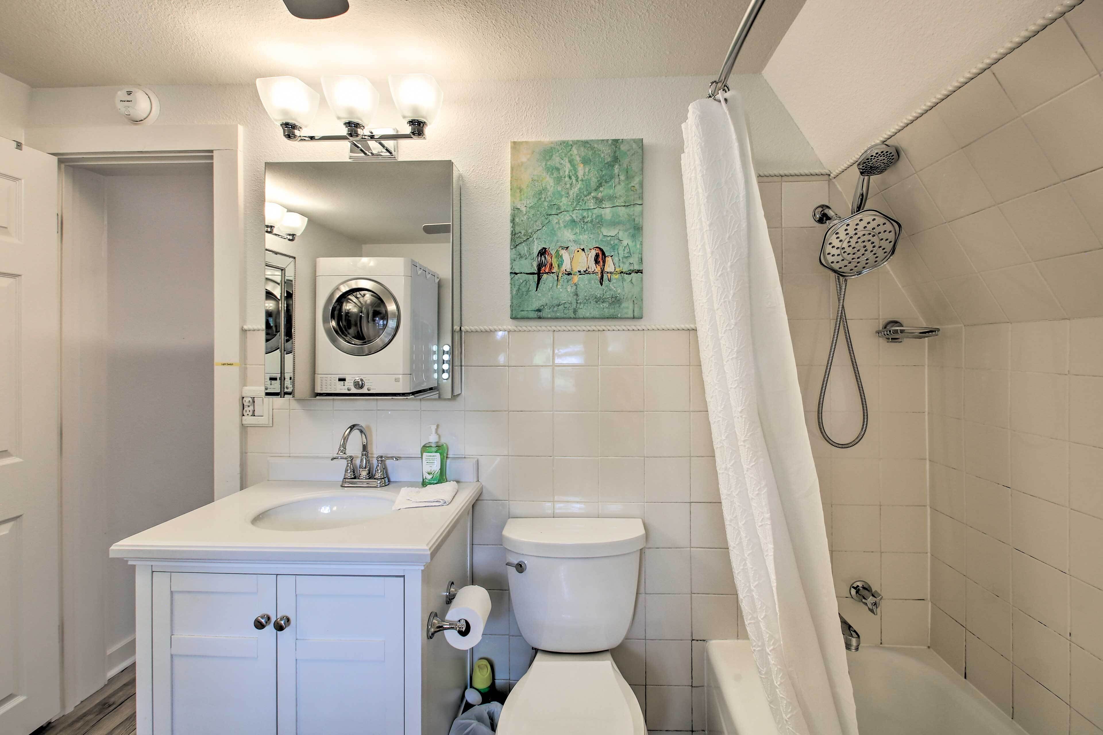 Un bagno con lavandino, toilette e doccia. Nell'angolo si trova una lavatrice e al muro un quadro.