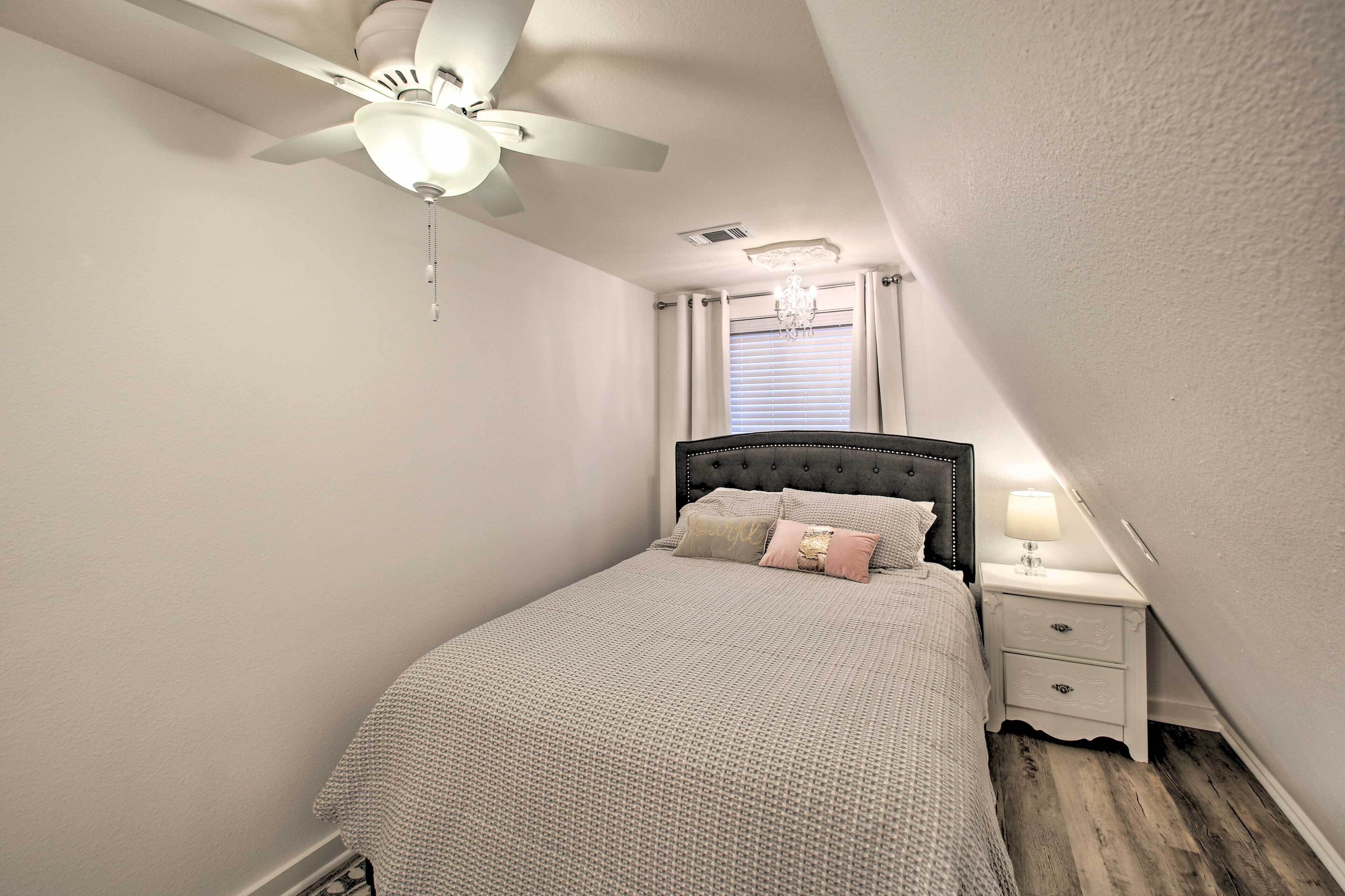 A bedroom with a bed, a nightstand, a ceiling fan, and a window with curtains.