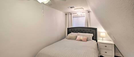 A bedroom with a bed, a nightstand, a ceiling fan, and a window with curtains.