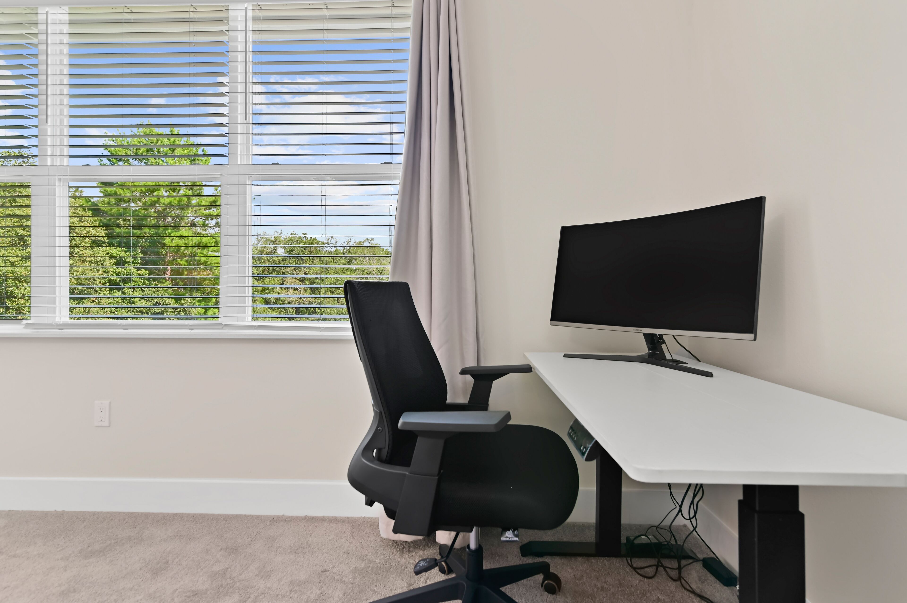 A room with a white desk, black office chair, and a flat-screen monitor.