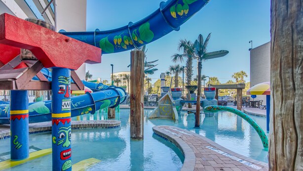 Un parque acuático con toboganes, piscinas, estructuras de madera y palmeras.