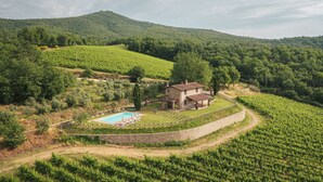 Une maison en pierre avec une piscine, entourée de vignes, située sur une colline.