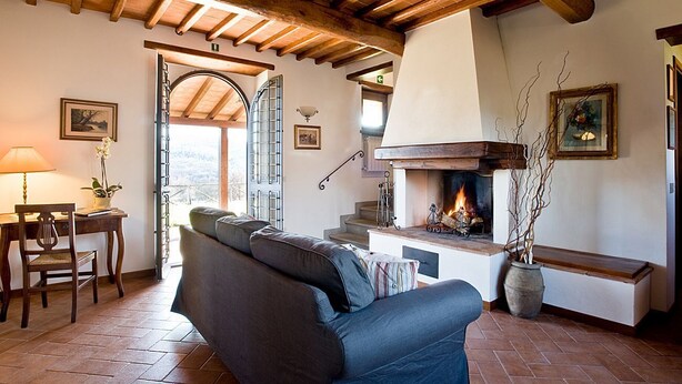 Un salon chaleureux avec une cheminée, un canapé, une table à manger avec des chaises et une vue dégagée grâce à une arche ouverte.