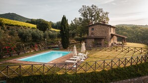 Une maison en pierre avec une piscine, entourée d’une clôture en bois et d’une végétation luxuriante.