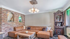 A living room with a brick wall, a wooden coffee table, a brown leather sofa, and a wooden cabinet with a glass door.