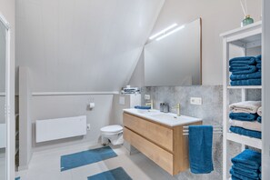 Un baño moderno con lavamanos blanco, tocador de madera y un perchero.
