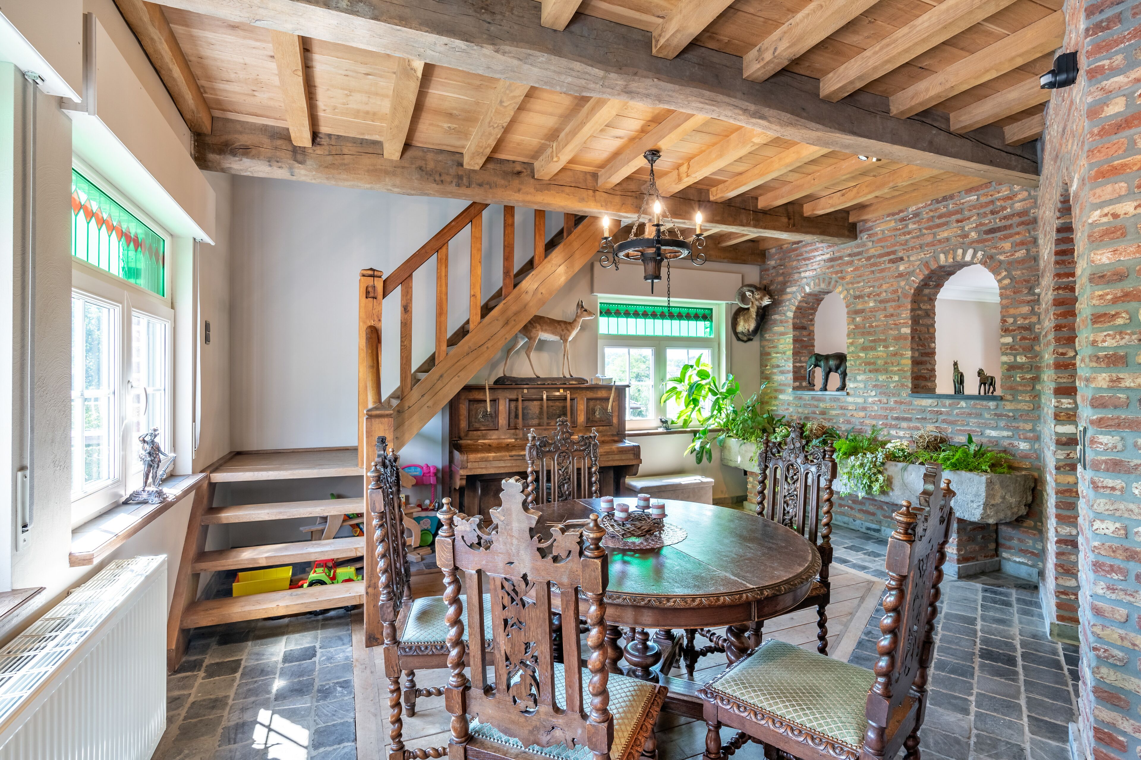Een eetruimte met een houten tafel en stoelen, een kroonluchter en een trap met houten leuning.