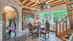 A dining area with a wooden table and chairs, a chandelier, and a brick wall.