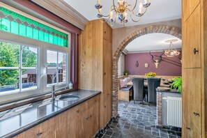 Una cocina con un ventanal grande, un lavamanos y una zona de comedor con mesa y sillas.