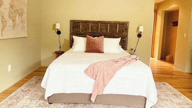 A neatly made bed with a wooden headboard, two bedside lamps, and a world map on the wall. - #2 Alder Queen Room - Fireplace in Olympic Nat'l Pk (Port Angeles)