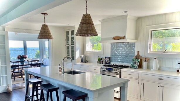 Una cocina moderna con una isla grande, armarios blancos y vista al océano.