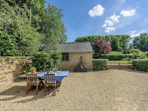 A stone building with a gravel patio, a table with chairs, and a small garden area.