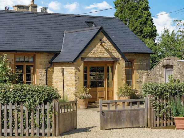 A stone building with a dark roof, wooden doors, and a gravel driveway.