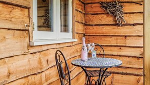 A wooden cabin with a window, a table with chairs, and a bottle of champagne. - 1 bedroom accommodation in Launcherley, near Wells (Launcherley, near Wells)