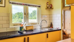 A kitchen with yellow cabinets, a black countertop, a window with a view of greenery, a sink, and a decorative rooster. - 1 bedroom accommodation in Launcherley, near Wells (Launcherley, near Wells)