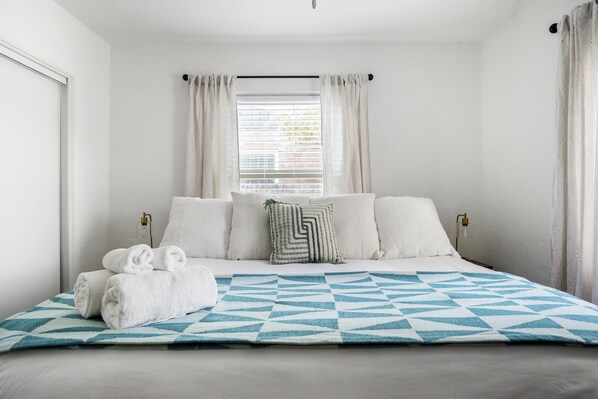 Una cama bien hecha con una colcha de estampado geométrico, almohadas blancas y un cojín decorativo.