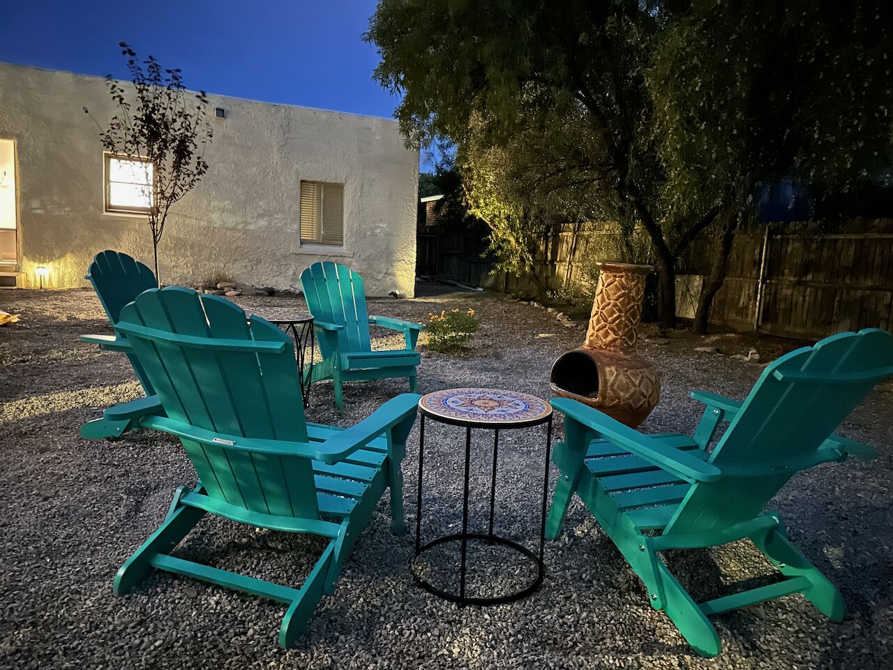 A patio with four green Adirondack chairs and a small round table with a patterned top.