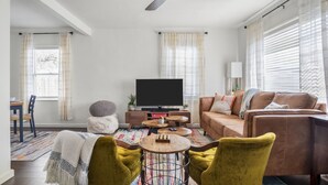 Uma sala de estar com sofá, duas poltronas, uma mesa de centro, televisão e ventilador de teto.