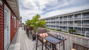 A balcony with wicker furniture and a potted plant, overlooking a multi-story building with balconies.