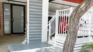 A covered outdoor area with a wooden deck, a metal railing, and a tree.