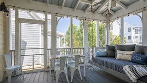 En inglasad veranda med ett bord och stolar, en soffa med kuddar och utsikt över kvarteret.
