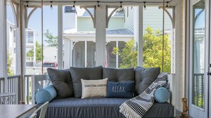 En veranda med en bekväm sittgrupp, ett bord och utsikt över ett hus och träd.